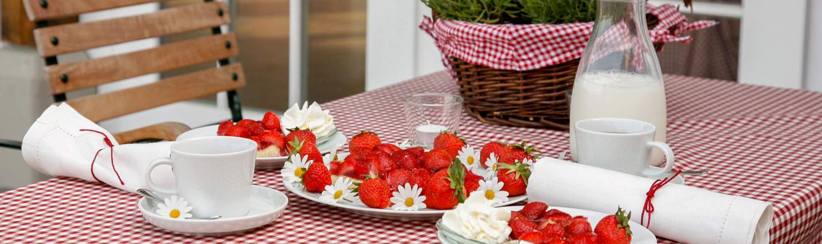 Tisch mit karierter Decke, Erdbeeren und einer Karaffe Milch