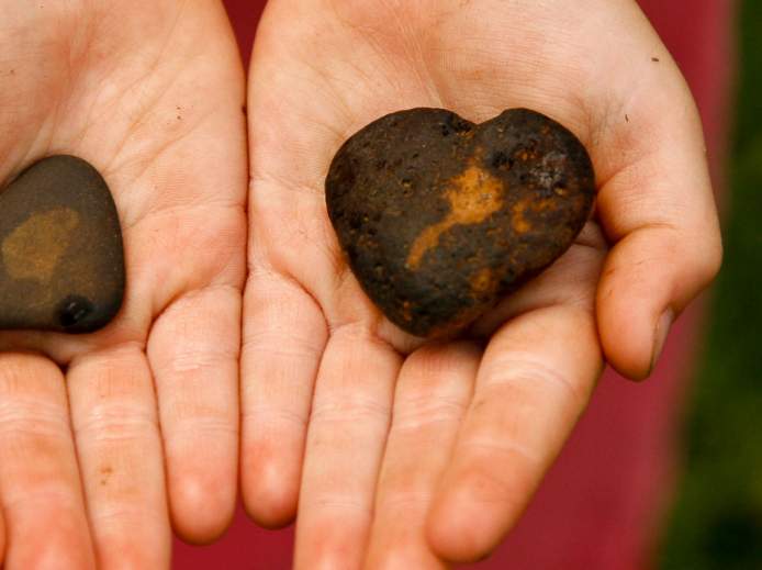 Zwei Hände zeigen Steine in Herzform